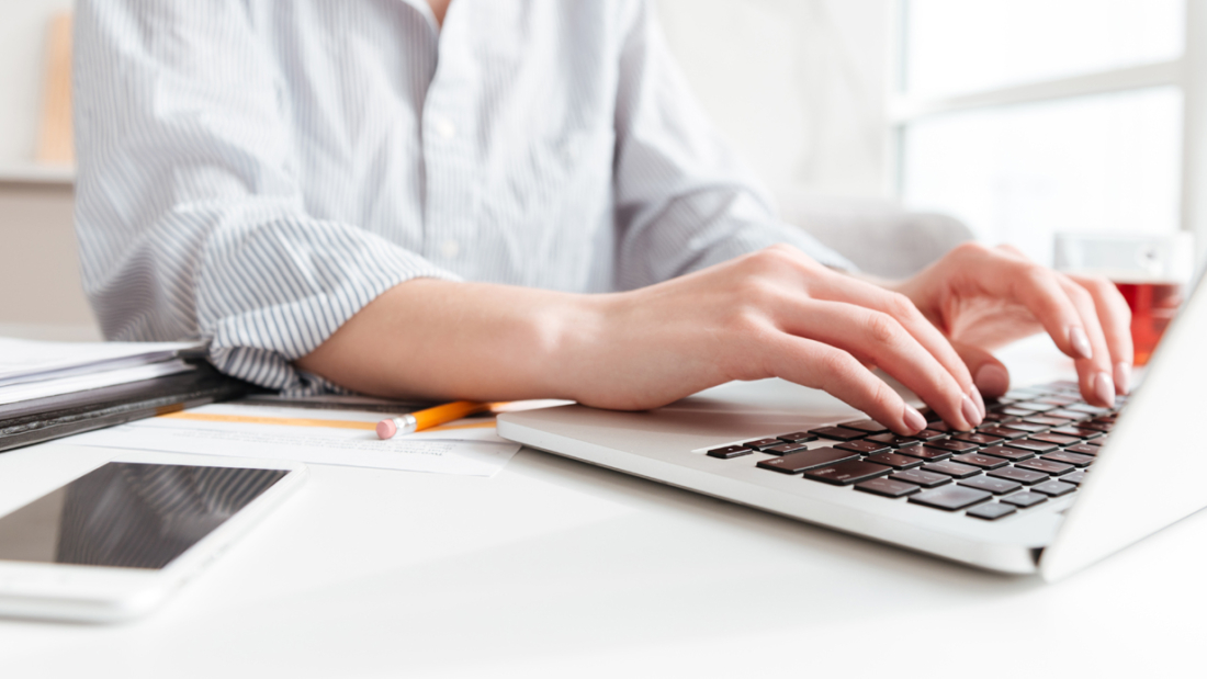Cropped photo of pretty brunette woman typing email on laptop computer while sitting at home, selective focus on hand